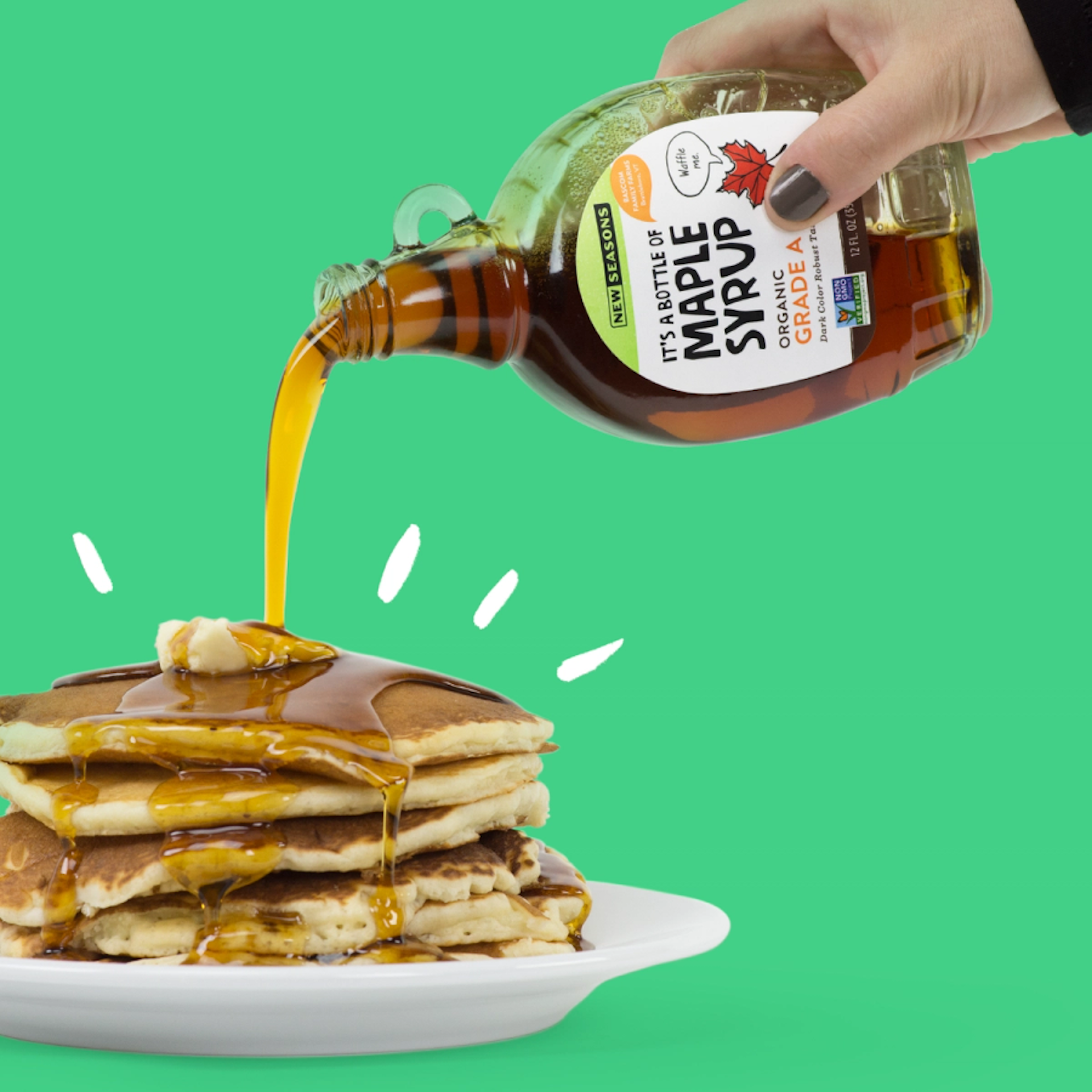 Person pouring maple syrup from a small glass container onto a stack of pancakes on a white plate, all in front of a green background