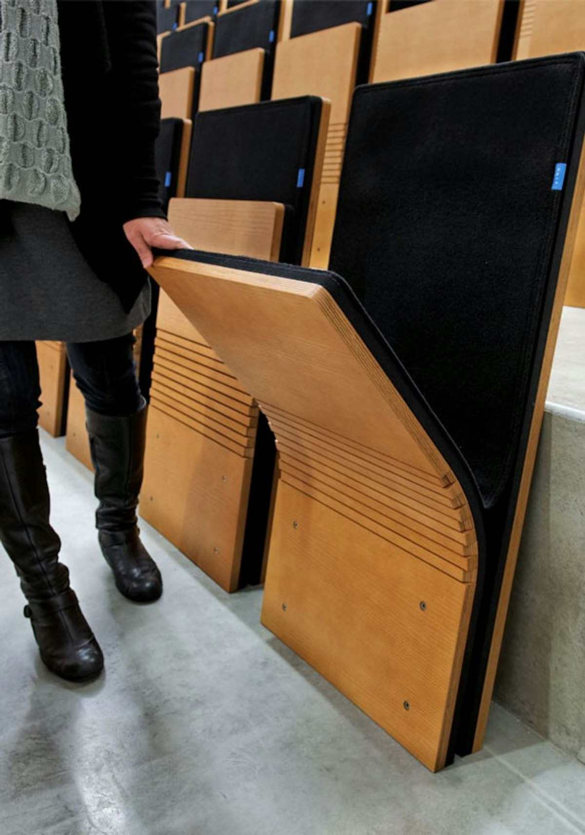 Woman in an auditorium filled with JumpSeats, pulling down a seat in preparation to sit.