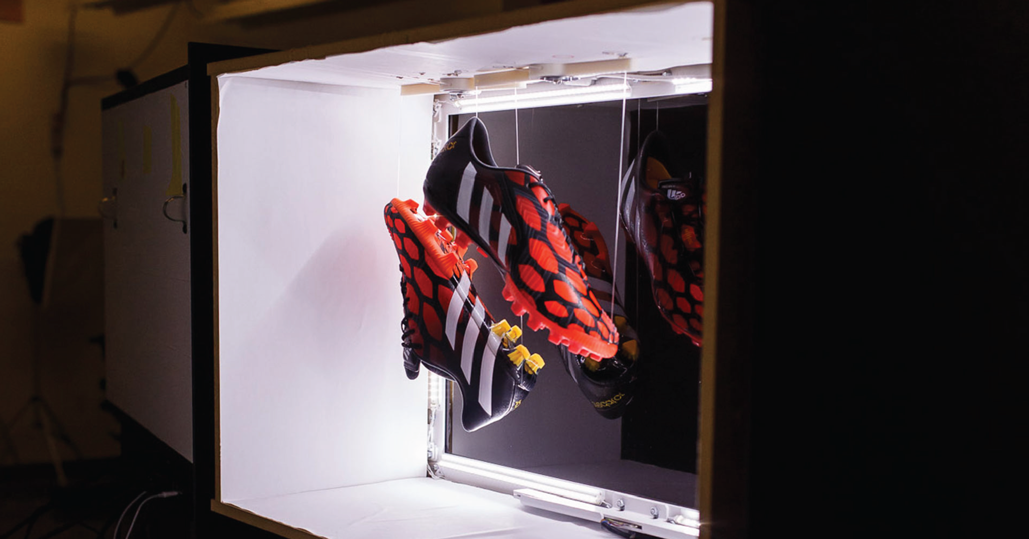 Two red cleats suspended on string inside of a white illuminated box